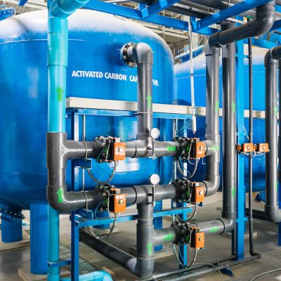 Large industrial water treatment and boiler room. Shiny steel metal pipes and blue pumps and valves.